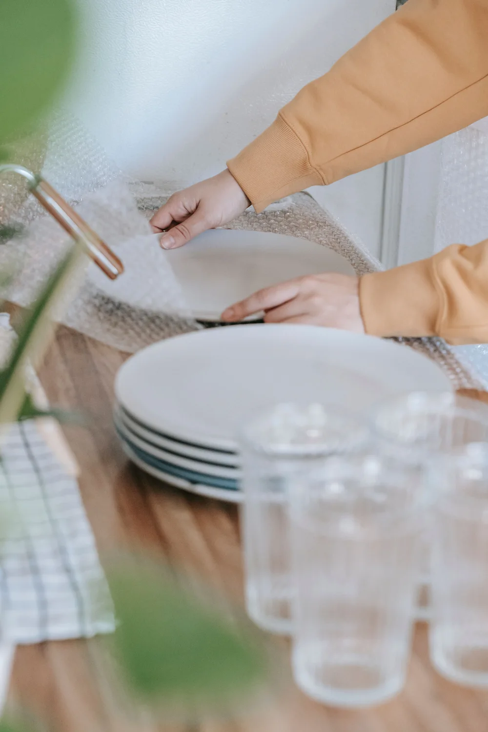 Close-up of hands carefully wrapping fragile ceramic plates in premium bubble wrap, showcasing the high-quality packing materials available from Atlantis Removals.