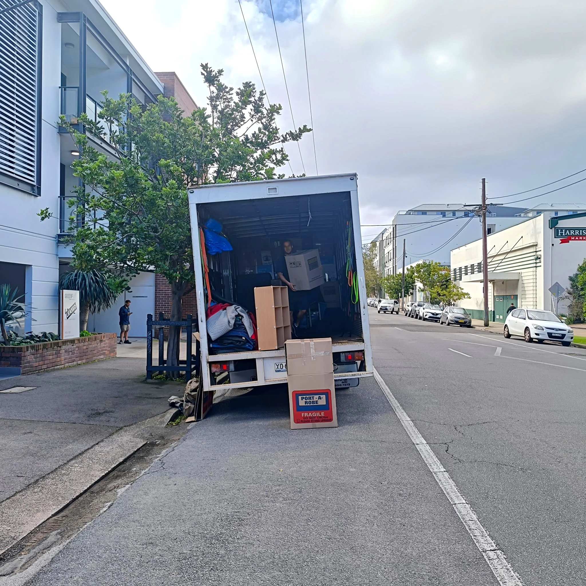 An Atlantis Removals truck parked safely on a busy street while navigating apartment access, showing why it's important to choose an experienced local moving company in Newcastle.