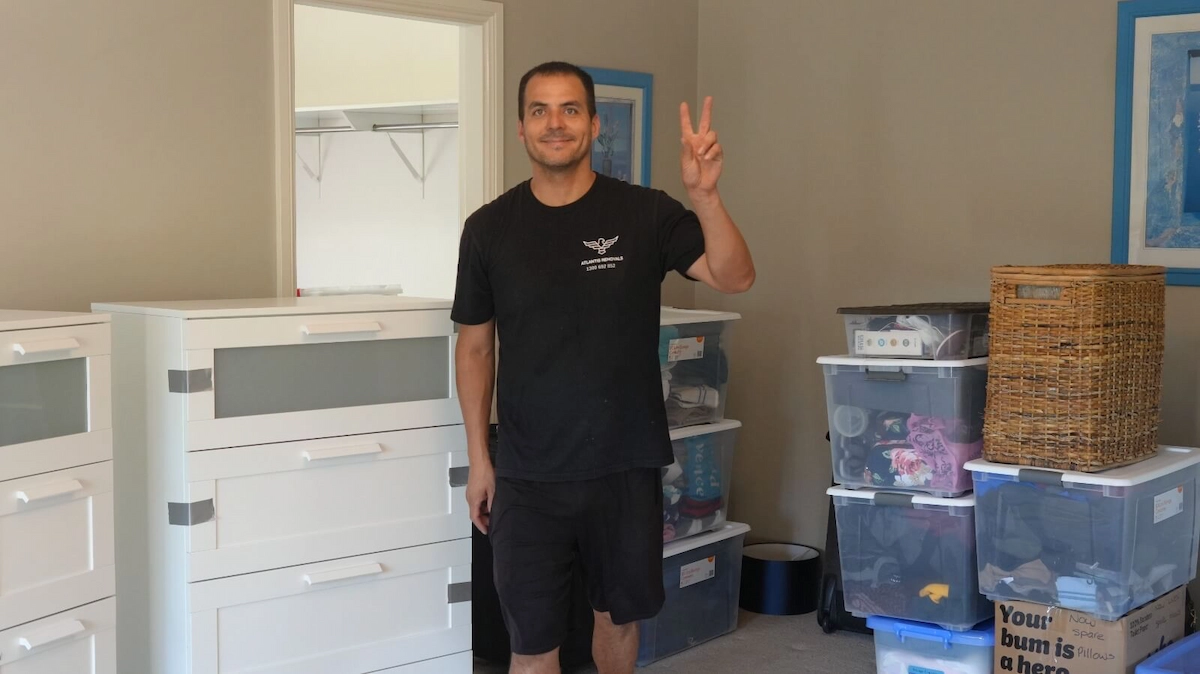 Friendly Atlantis Removals team member smiling and giving a peace sign in a room filled with packed moving boxes.