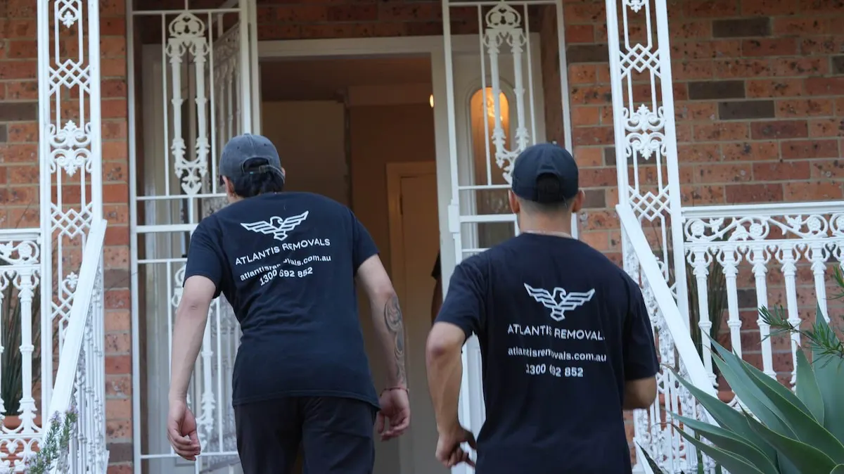 Two Atlantis Removals team members in uniform walking up the steps to a brick house for a local residential move in Newcastle.