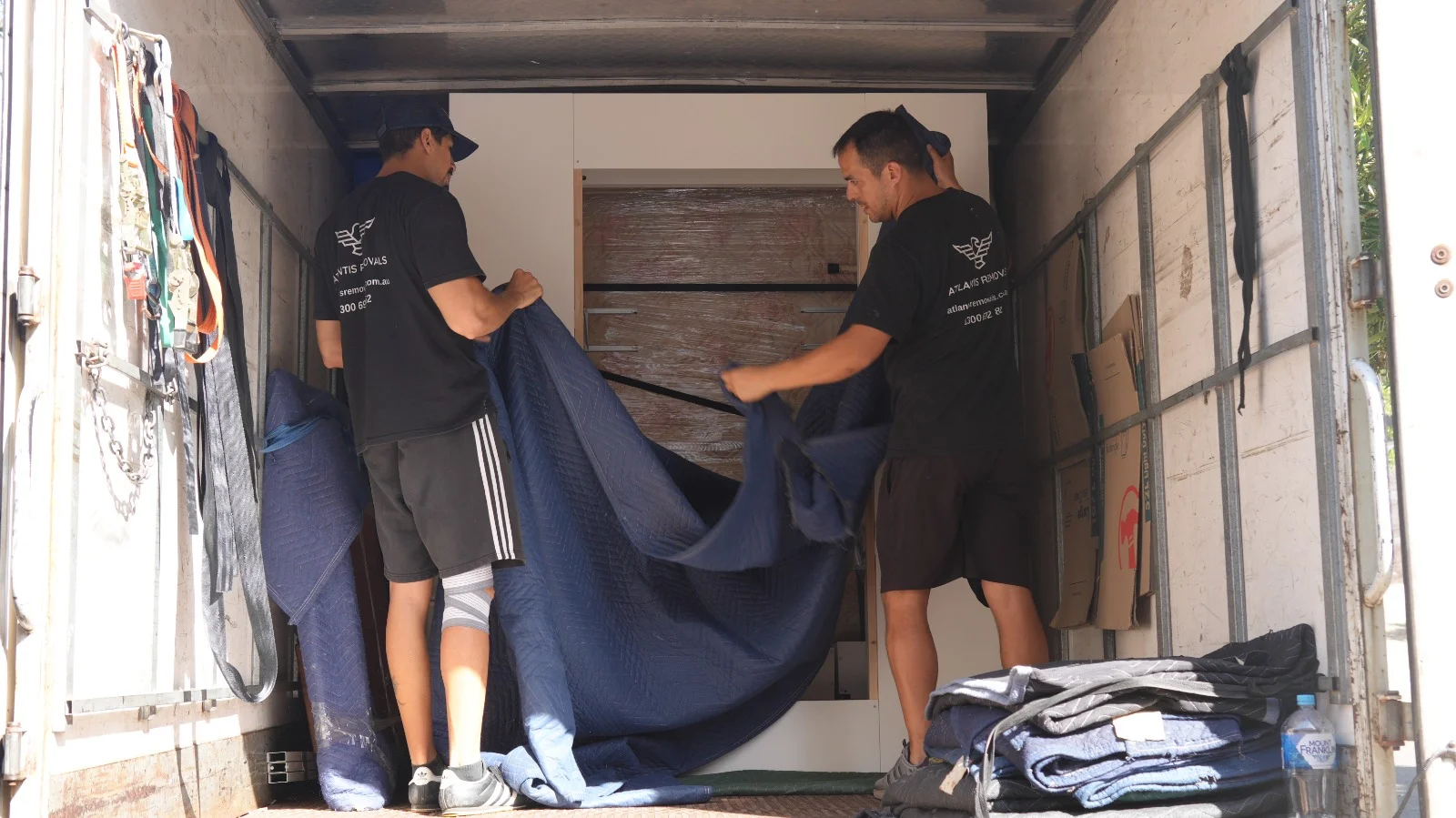 Atlantis Removals team members using a heavy blue moving blanket to protect furniture inside a truck for a safe Sydney to Newcastle relocation.