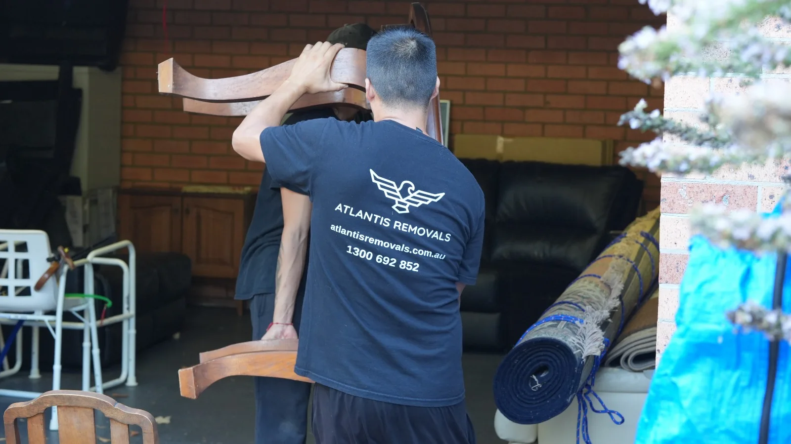 Atlantis Removals team member in a branded uniform carefully carrying a large piece of wooden furniture during a relocation between Sydney and Lake Macquarie.
