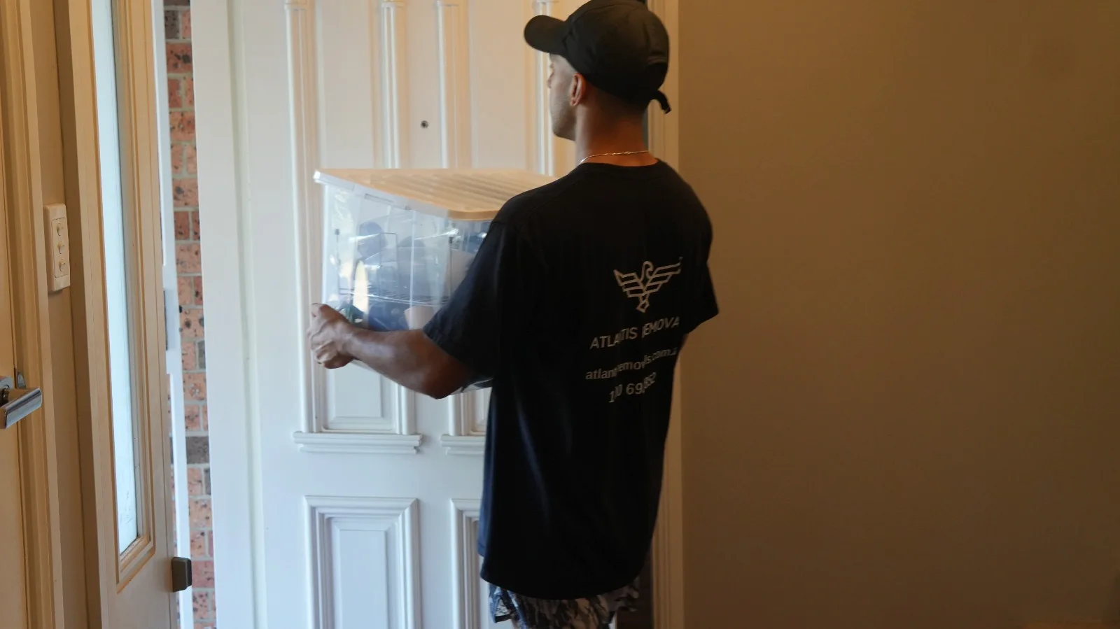 Atlantis Removals team member in a branded uniform carefully carrying a clear moving tub through a doorway during a relocation between Sydney and Maitland.